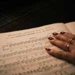 Woman's hand resting on sheet music — Foto por Maksim Zinchenko na Unsplash