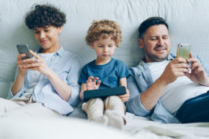 a man, woman and child sitting on a couch looking at their cell phones — Foto por Vitaly Gariev na Unsplash