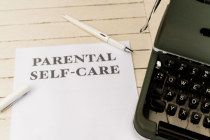a piece of paper that says parental self - care next to a typewriter — Foto por Markus Winkler na Unsplash