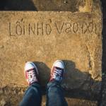 a person standing on a sidewalk with their feet up — Foto por Tien Vu Ngoc na Unsplash