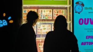 Two people look at a brightly lit vending machine. — Foto por Antoine Pouligny na Unsplash